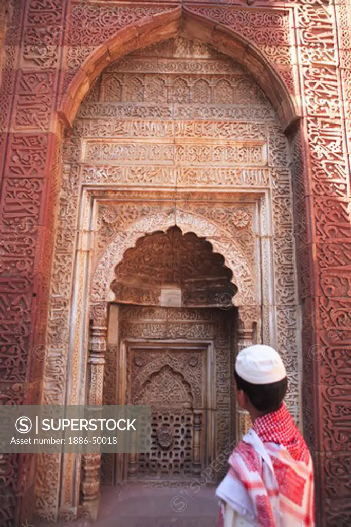 Muslim boy watching Islamic Ornamentation of Quran inscription carved on Qutab Minar complex built in 1311 red sandstone tower; Indo-Muslim art ; Delhi sultanate ; Delhi ; India UNESCO World Heritage Site
