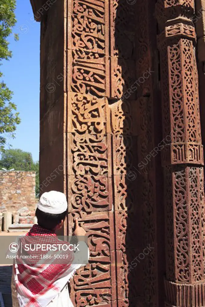 Muslim boy watching Islamic Ornamentation of Quran inscription carved on Qutab Minar complex built in 1311 red sandstone tower; Indo-Muslim art ; Delhi sultanate ; Delhi ; India UNESCO World Heritage Site