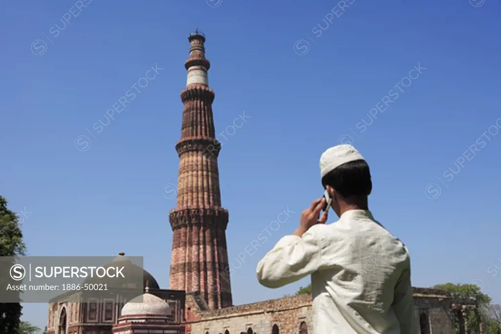 Muslim boy talking on mobile phone at Qutab Minar built in 1311 red sandstone tower; Indo-Muslim art ; Delhi sultanate ; Delhi ; India UNESCO World Heritage Site