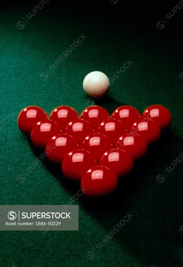 Red billiard balls and white cue ball laying on pool table in a triangular shape.