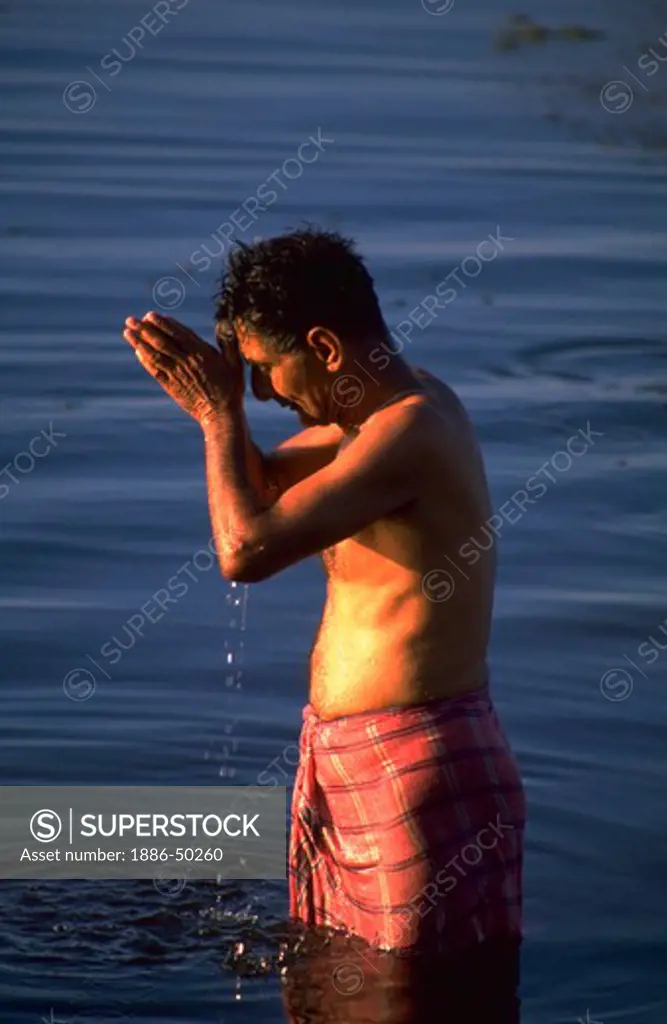 Hindu brahmin man worshipping the sun god by bathing in a river, India.