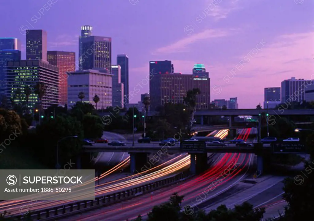 Los Angeles skyline at sunset with blurred lights of traffic on freeway.