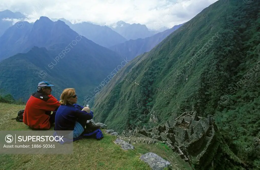 Two hikers relaxing on a hill above the Inca ruins of Winay Wayna, Peru.