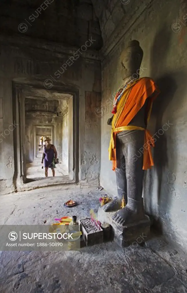 Tourist approaches a stone carved statue of the Hindu god Vishnu in the outer gopura of Angkor Wat, built in the 11th century by Suryavarman the 2nd,  -  Cambodia