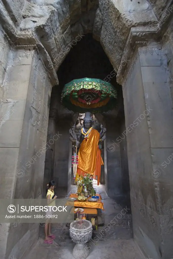 Cambodian girl worships at a stone carved statue of the Hindu god Vishnu in the outer gopura of Angkor Wat, built in the 11th century by Suryavarman the 2nd,  -  Cambodia