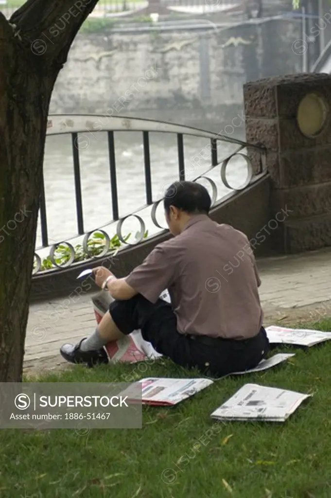 Man reads newspaper in a park along the Jin River - Chengdu, China in Sichuan Province