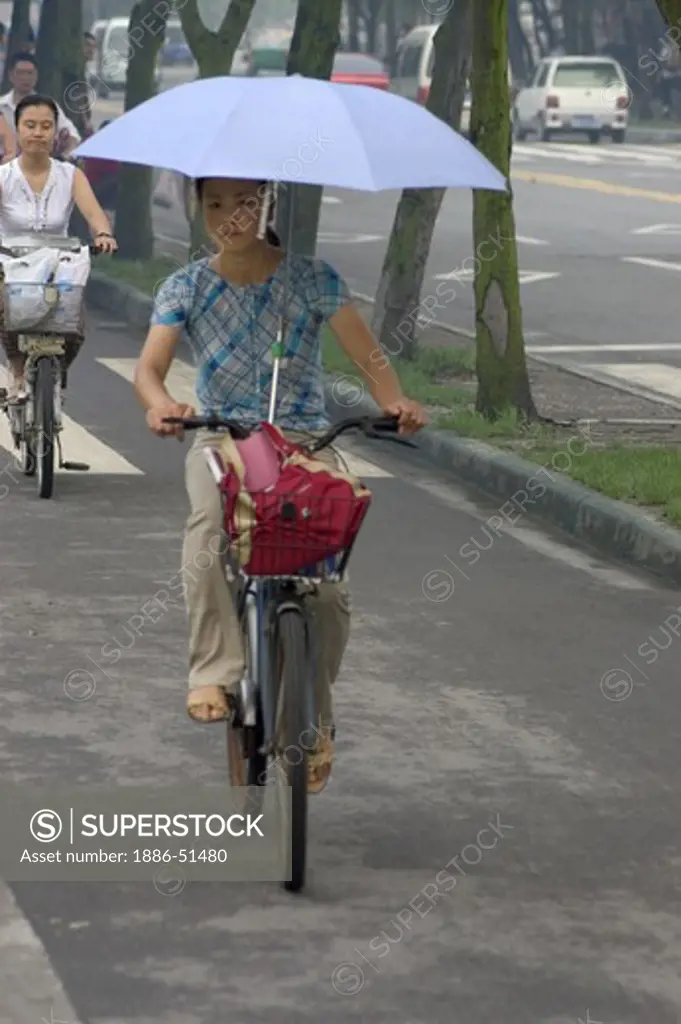 Woman rides a bicycle while using an umbrella against the rain - Chengdu, China in Sichuan Province
