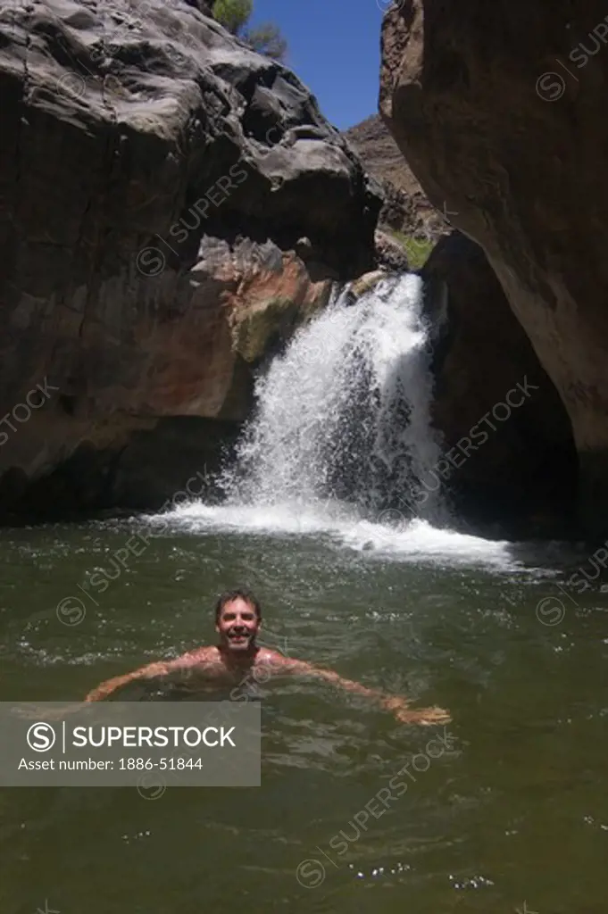 Raft guide Todd Lovell enjoys a swim below the waterfall at SHINOMU CREEK  at mile 108 along the Colorado River - GRAND CANYON, ARIZONA