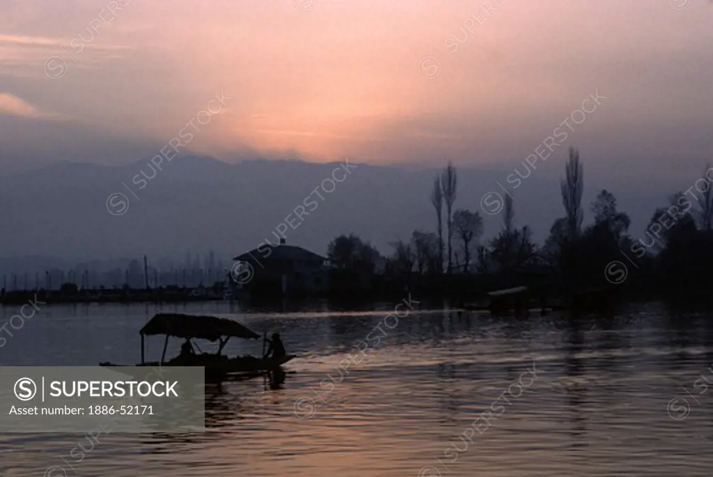 A SHIKARA, paddle boat with a canopy, floats across the tranquil waters of DAL LAKE at SUNRISE - KASHMIR, INDIA