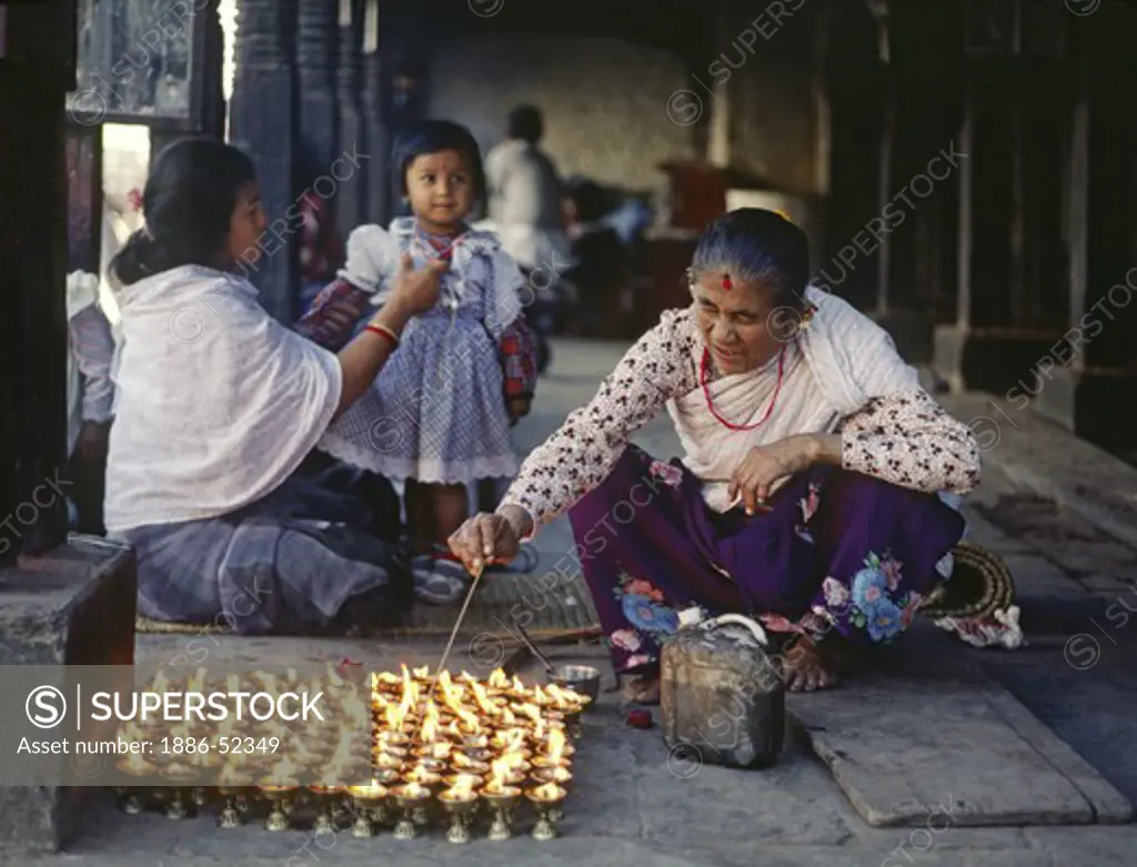 A NEWARI woman lights PUJA CANDLES at SWAYAMBUNATH STUPA - KATHAMANDU, NEPAL
