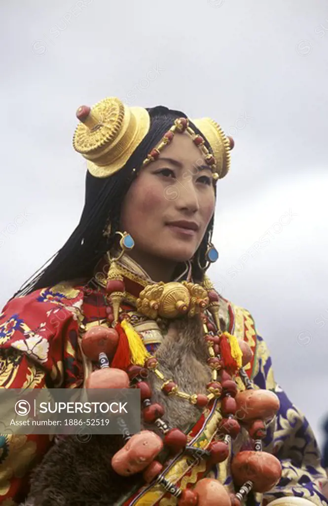 Female Khampa wears gold hair pieces & gau boxes, zee stones & coral at the Litang Horse Festival - Sichuan Province, China