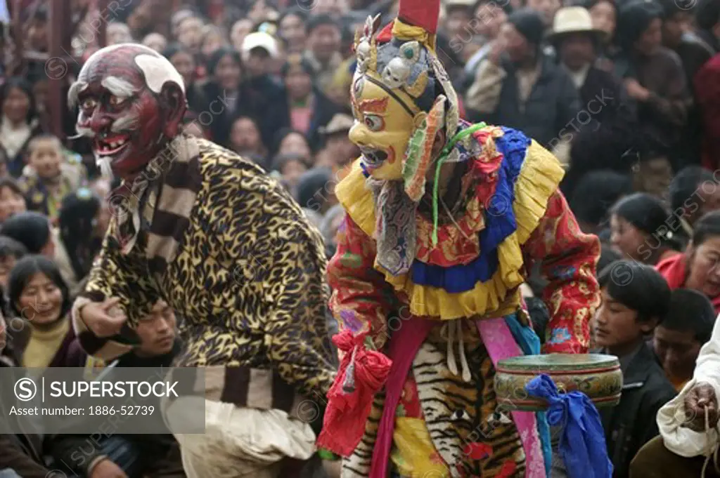 Masked dancer & clown entertain the crowd at the Monlam Chenmo masked dances, Katok Monastery - Kham, (Tibet), Sichuan, China