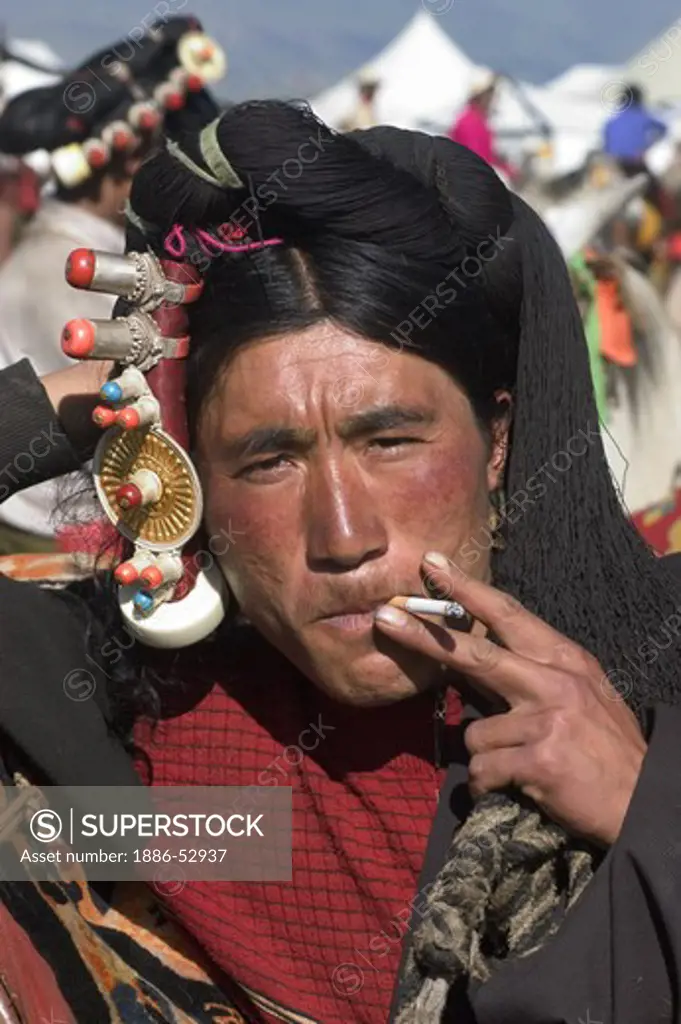 Khampa man with gold & coral hair peices smokes at the Litang Horse Festival - Kham, Sichuan Province, China, (Tibet)
