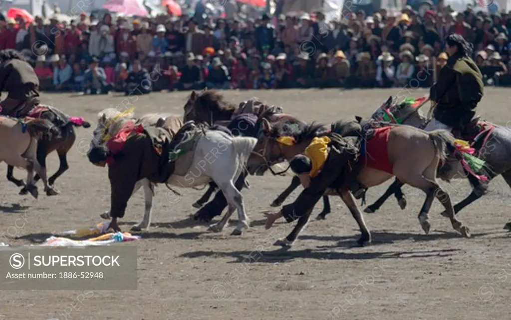 Khampas pick up Kathoks from the ground on horseback at the Litang Horse Festival in Kham - Sichuan Province, China, (Tibet)