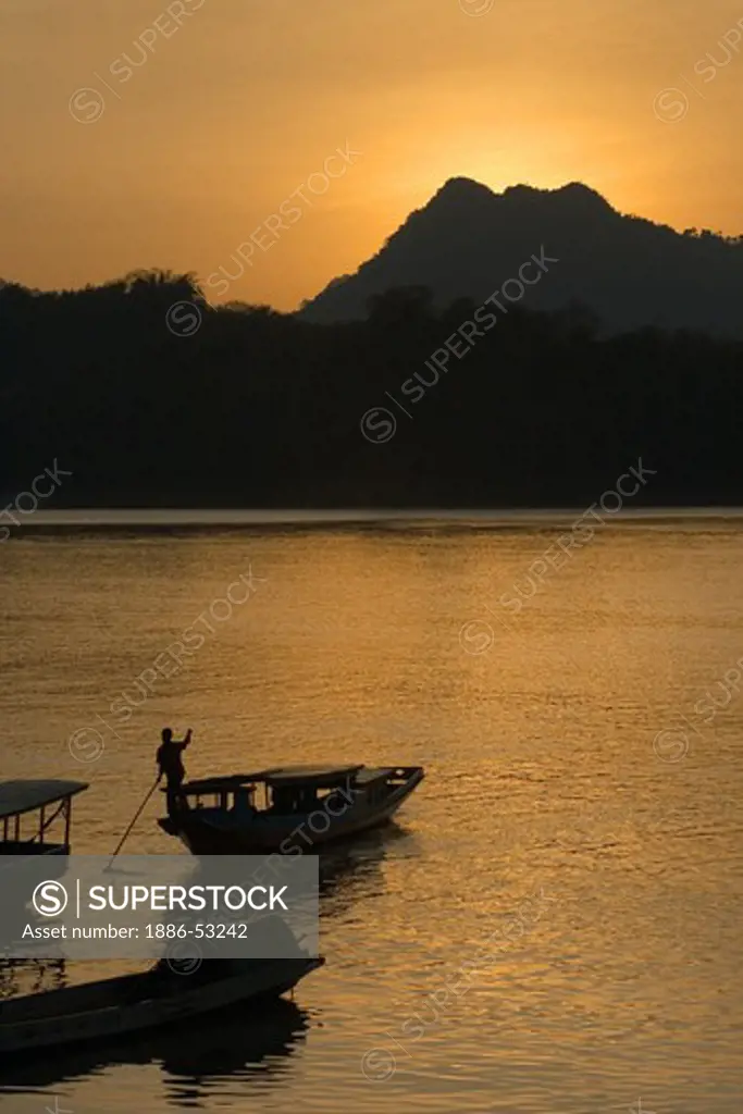The sunsets on the Mekong River silhouetting a slow boat which is used for transportation - LUANG PROBANG, LAOS