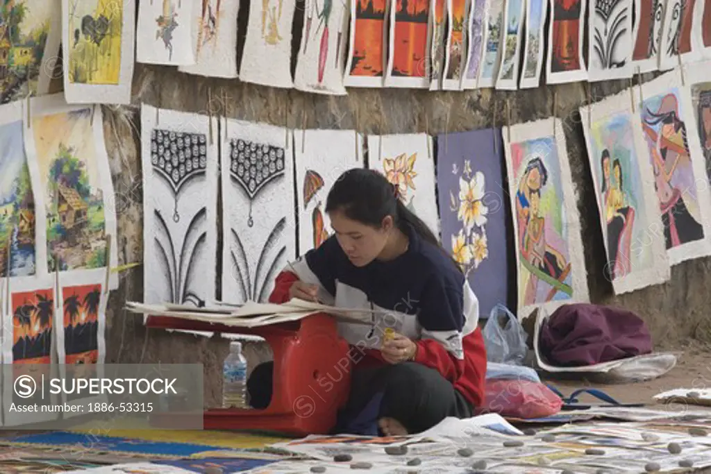A painter sells her paintings of local scenes are offered for sale in the once French Provincial town of LUANG PROBANG - LAOS