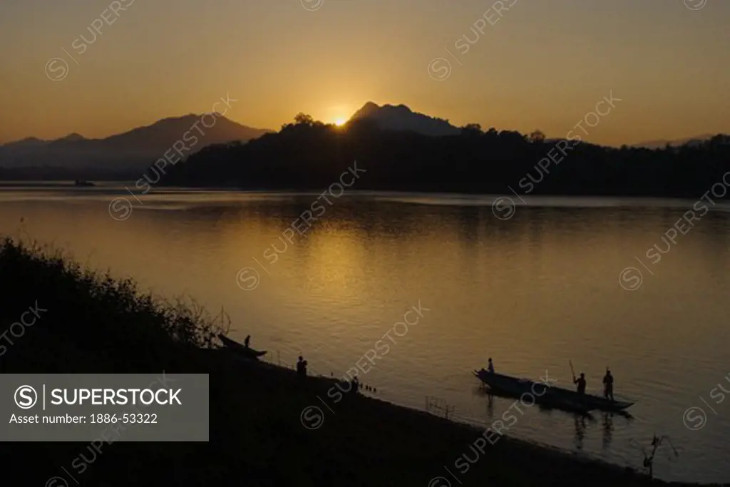 The sun sets over a hill on the Mekong River silhouetting a river boat as it runs through  - LUANG PROBANG,  LAOS