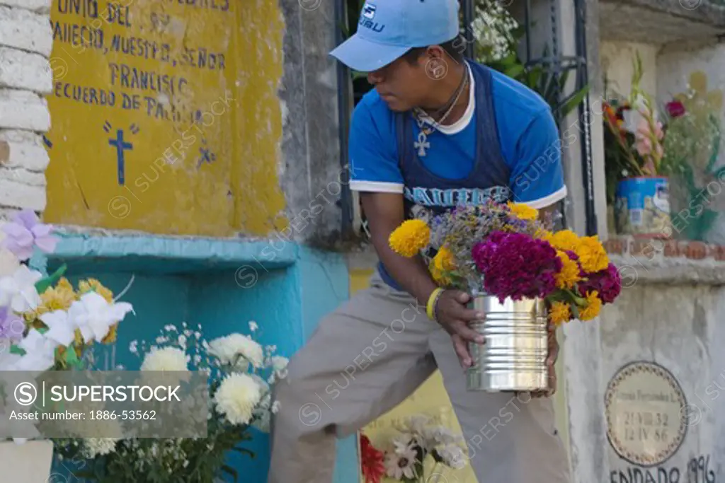 A young man places flowers on a relatives grave at the local cemetery during the DEAD OF THE DEAD - SAN MIGUEL DE ALLENDE, MEXICO