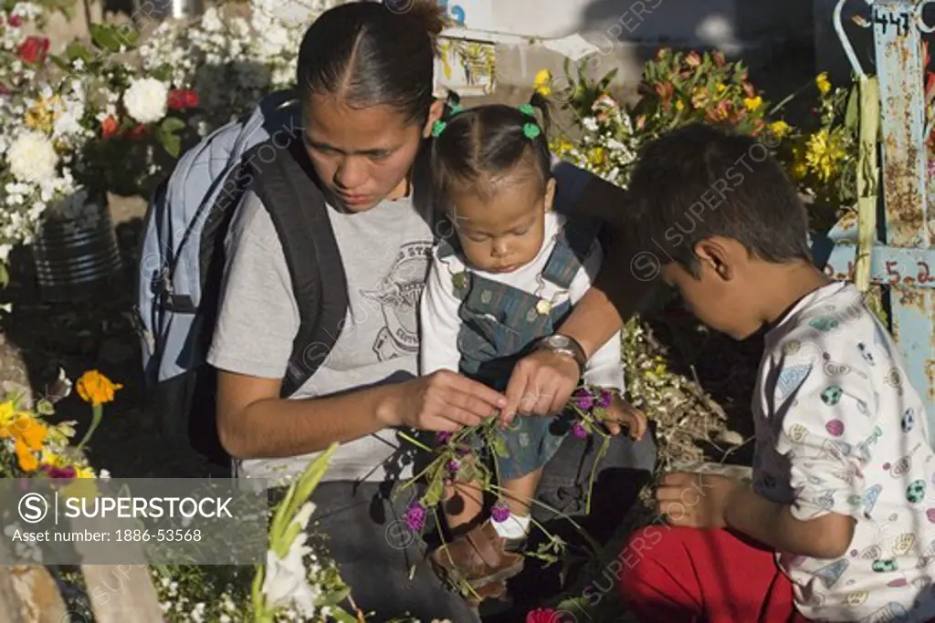 A young family arrange flowers on a grave at the local cemetery during the DEAD OF THE DEAD - SAN MIGUEL DE ALLENDE, MEXICO