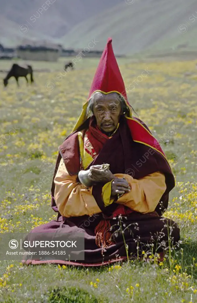 HEAD MONK of JAGLUNG Monastery holds a bell and dorje in a flowery Himalayan field, DO TARAP VALLEY - DOLPO DISTRICT, NEPAL
