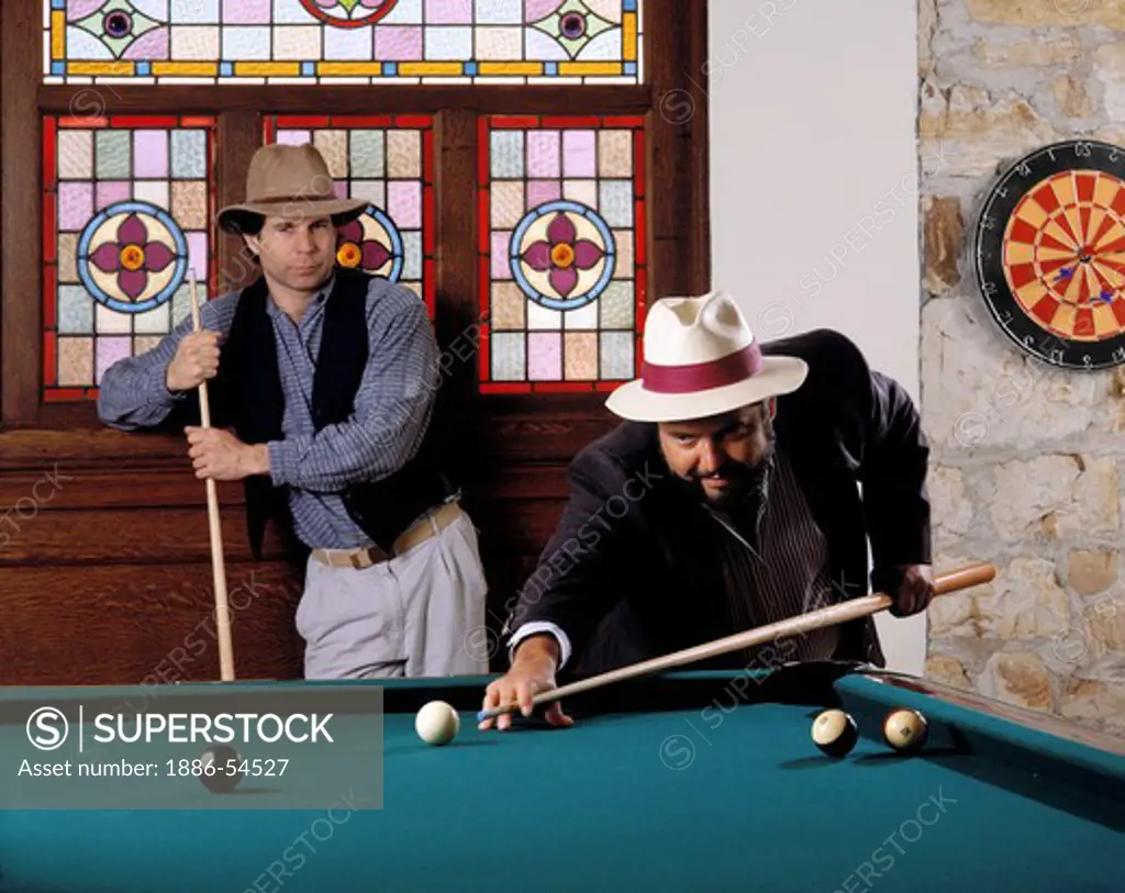Stylishly dressed opponents sporting hats play BILLIARDS in a private recreation room - model released