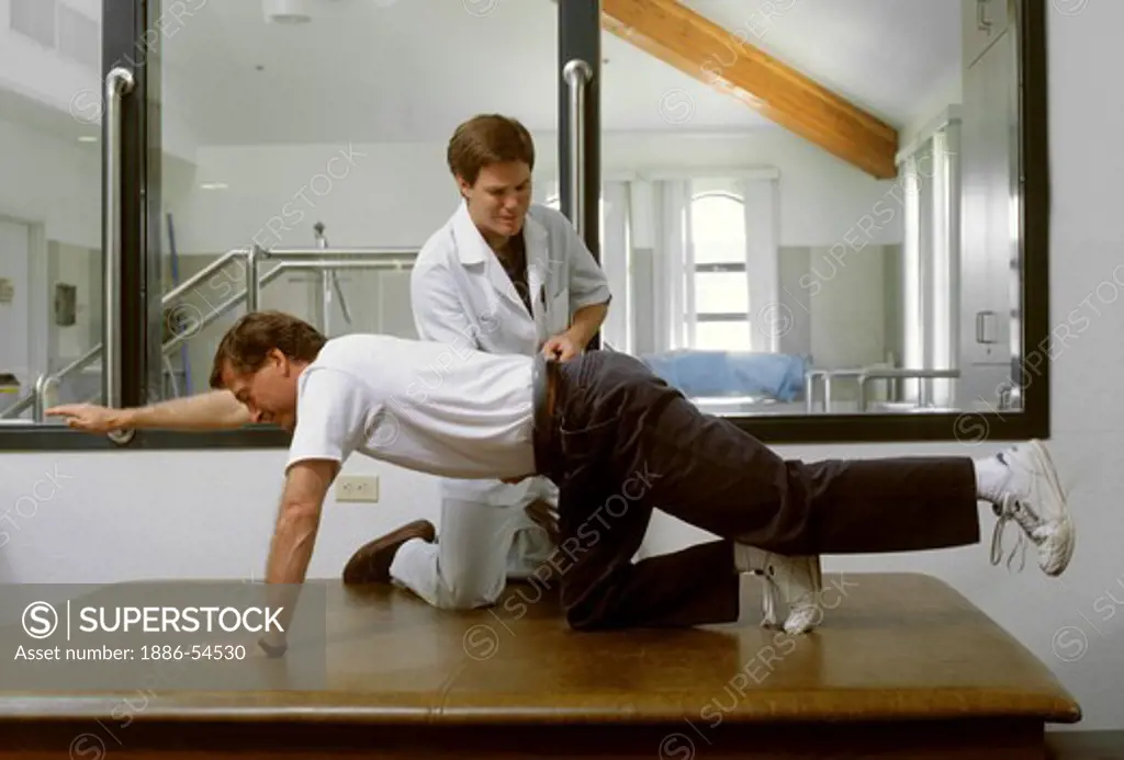 A PHYSICAL THERAPIST shows a male patient some exercises at a PHYSICAL THERAPY FACILITY