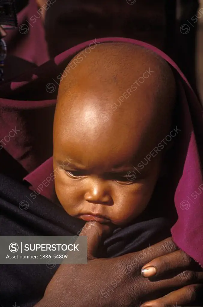A MASSAI child is held in her mothers arms in her village near the rim of NGORONGORO CRATER - TANZANIA, AFRICA