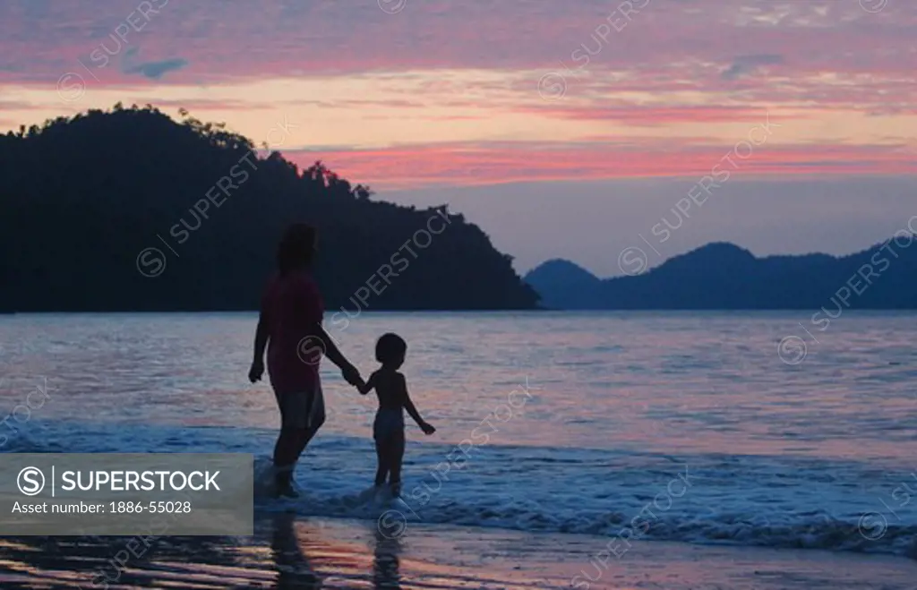 Sunset over the North Andaman Sea silhouettes a Thai mother and child enjoying the moment at Hat Prapat Beach - KURABURI, THAILAND