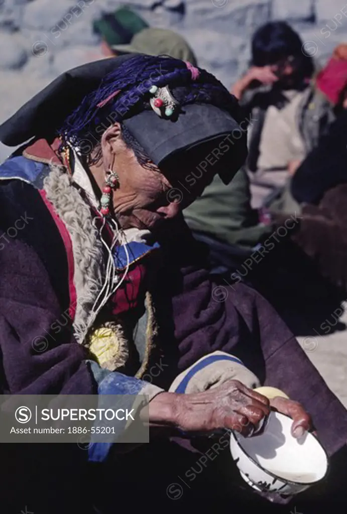 Tibetan pilgrim with fine jewelry washes her eating bowl - Sakya, Tibet