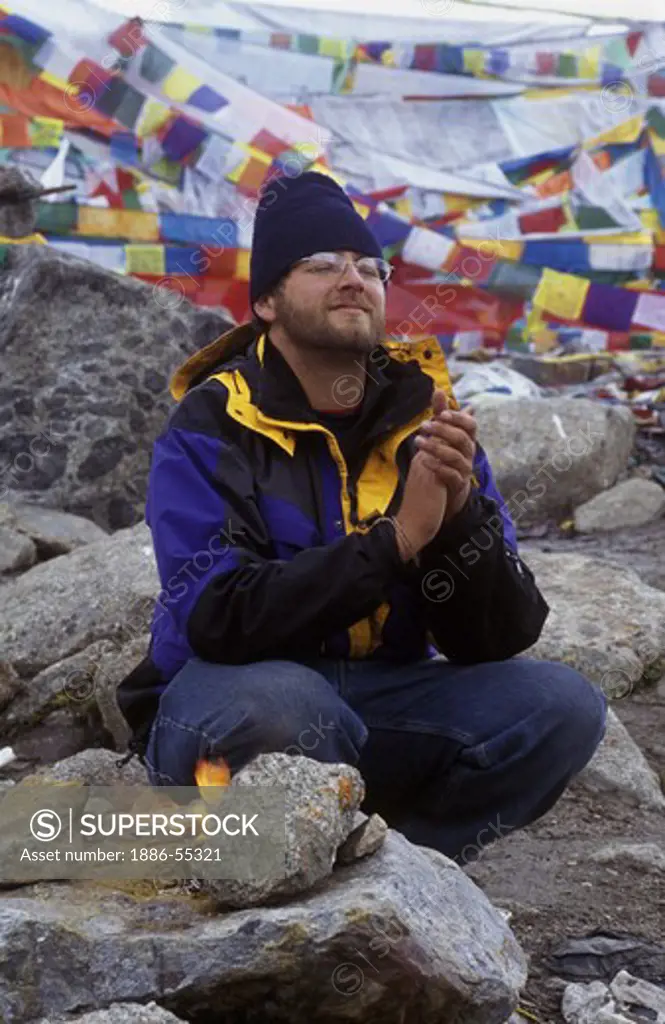 American man prays atop the DOLMA LA (18,395 ft.), the highest point of the KORA around MOUNT KAILASH, TIBET