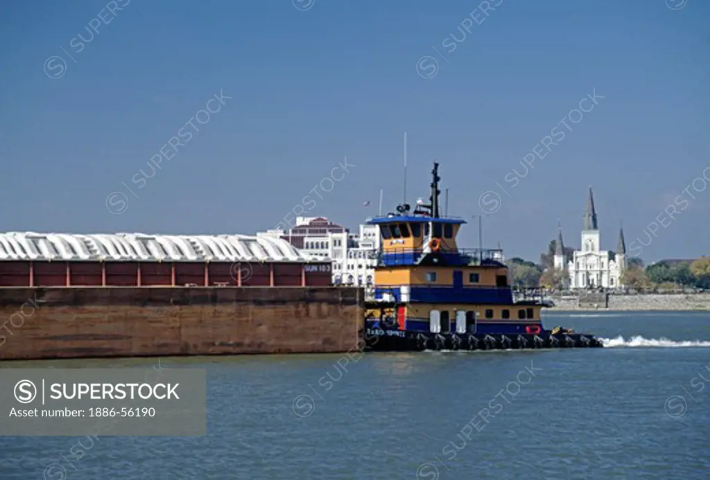 A TUG BOAT pushes a barge along the MISSISSIPPI RIVER as it winds past ST LOUIS CATHEDRAL in the FRENCH QUARTER - NEW ORLEANS, LOUISIANA