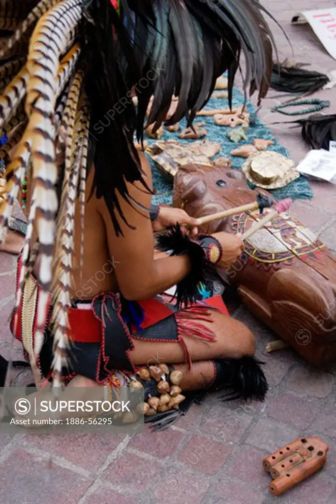 An AZTEC DANCER plays a DRUM dressed in a traditional warrior feathered COSTUME  during the CERVANTINO FESTIVAL  - GUANAJUATO, MEXICO
