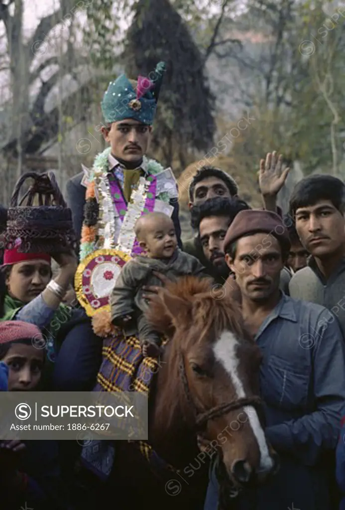 COSTUMED GROOM rides a HORSE to his brides home in AFAN VILLAGE during his WEDDING - KASHMIR, INDIA 