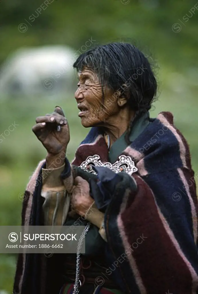 OLD WOMAN SMOKING cigarrette in DOLPO BLANKET at a Tibetan Buddhist FESTIVAL in DO TARAP VALLEY - DOLPO DISTRICT, NEPAL