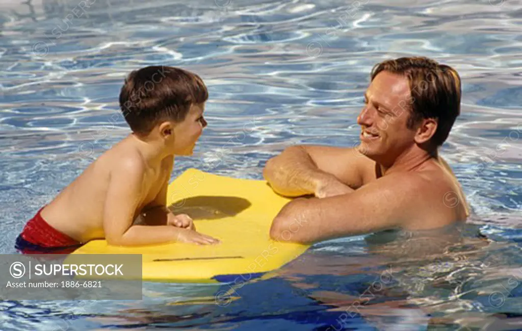 A father place with his five year old son who is floating on a Moray Boogy Board in a swimming pool.