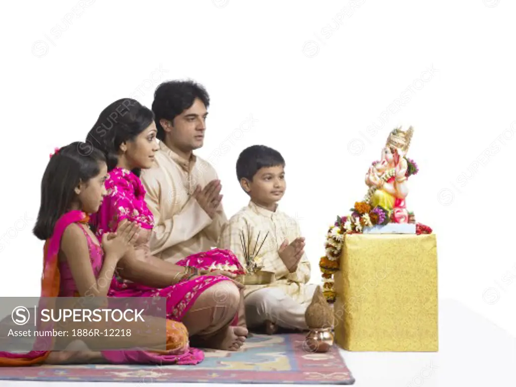 VDA200245 : South Asian Indian family with father, mother, son and daughter sitting praying to lord Ganesha wearing traditional dress kurta, pajama, pink and orange color dress, pink dress, MR # 698, 699, 700, 701