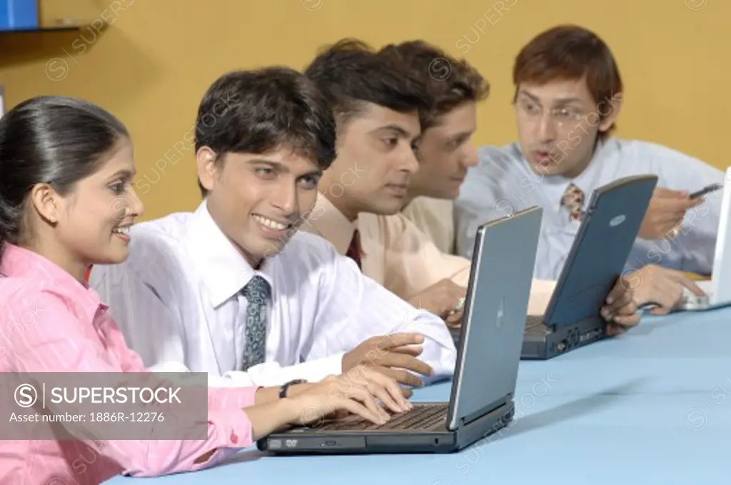 MAK200690 : South Asian Indian businessmen and woman sitting in conference room,  smiling and working on laptop,  conversation to each other wearing blue shirt,  pink shirt,  white shirt and tie in Office MR # 670D,  670E,  670F, 670G,  670H