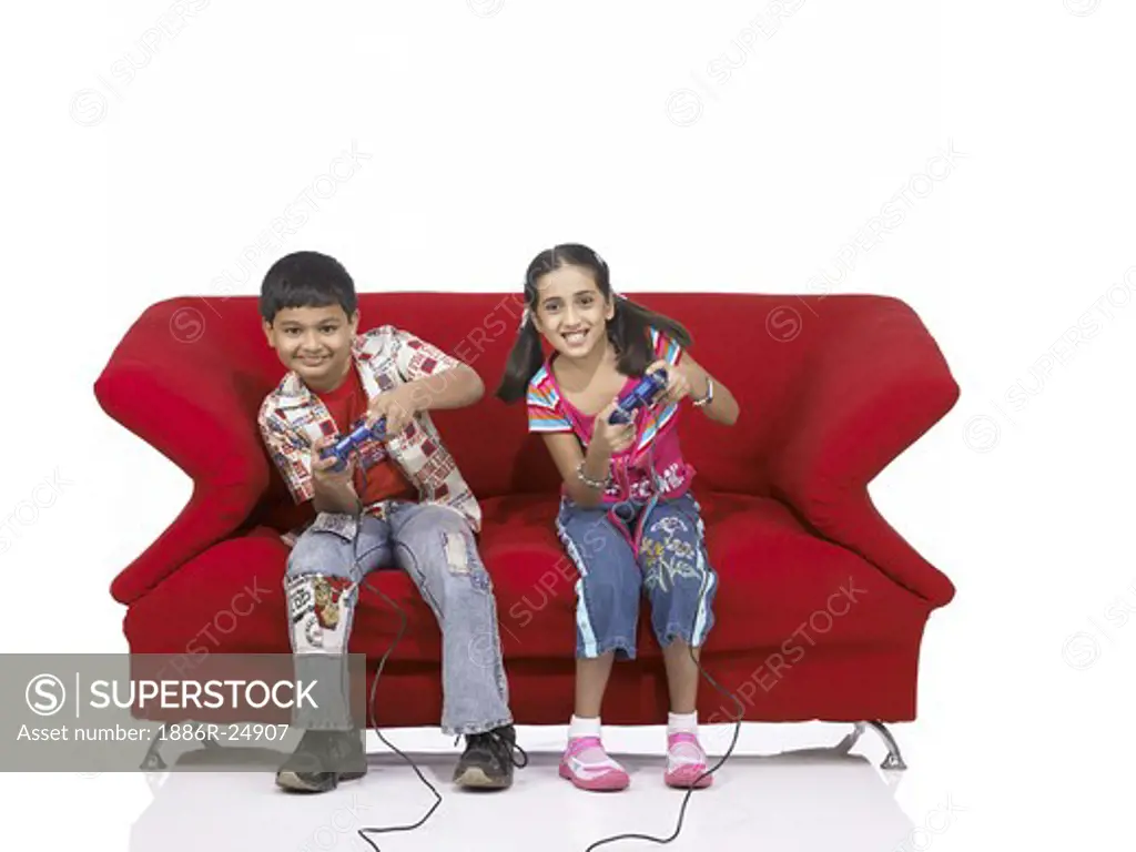 VDA200174 : South Asian Indian two children brother and sister sitting on sofa playing video game wearing jeans and shirt, MR #  699, 700