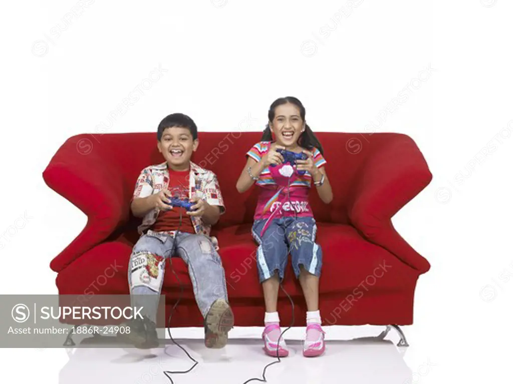 VDA200175 : South Asian Indian two children brother and sister sitting on sofa playing video game wearing jeans and shirt, MR #  699, 700
