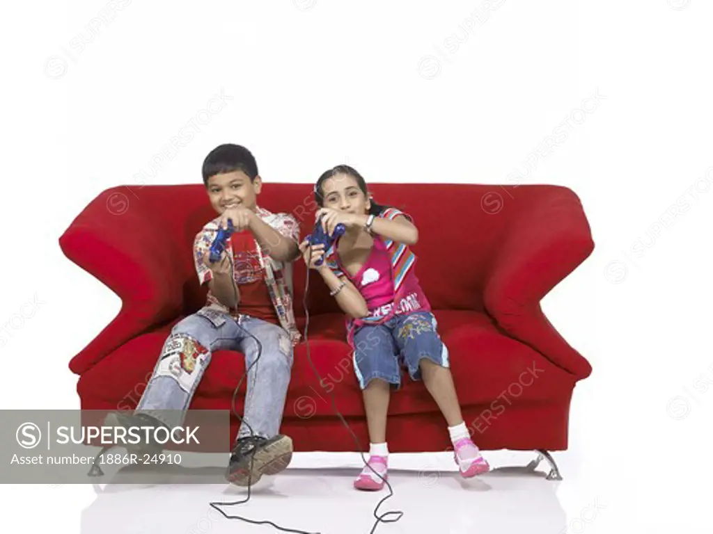 VDA200177 : South Asian Indian two children brother and sister sitting on sofa playing video game wearing jeans and shirt, MR #  699, 700