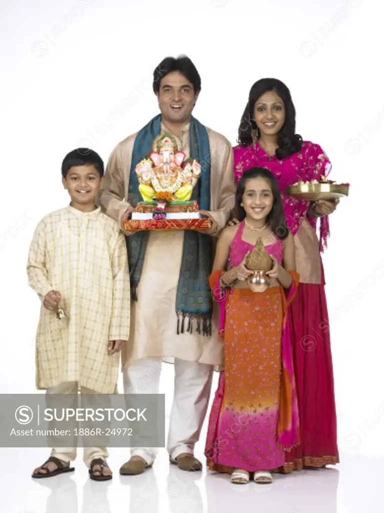 VDA200270 : South Asian Indian family with father, mother, son and daughter standing smiling, holding statue of lord Ganesha, Kalash, Arati thali and looking at camera wearing traditional dress kurta, pajama, pink and orange color dress, pink dress, MR # 698, 699, 700, 701