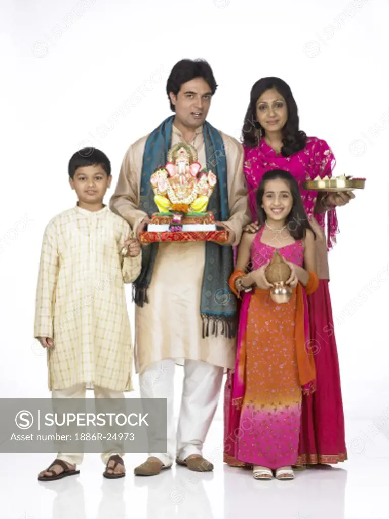 VDA200272 : South Asian Indian family with father, mother, son and daughter standing smiling, holding statue of lord Ganesha, Kalash, Arati thali and looking at camera wearing traditional dress kurta, pajama, pink and orange color dress, pink dress, MR # 698, 699, 700, 701