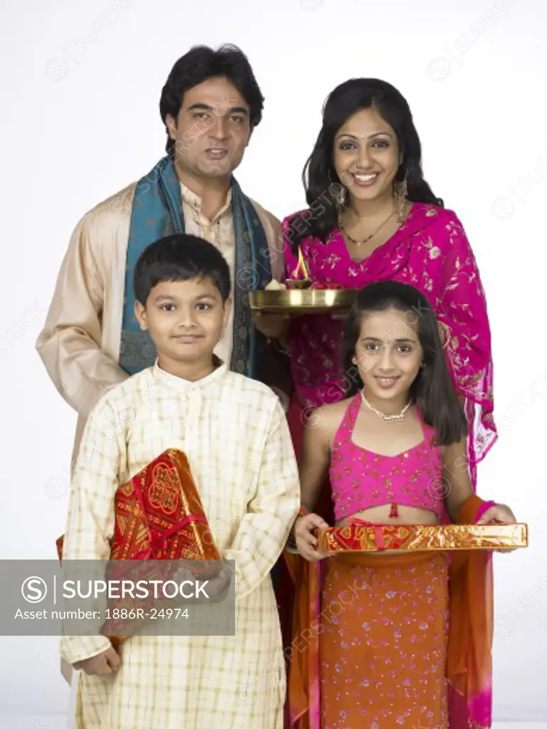 VDA200274 : South Asian Indian family with father, mother, son and daughter standing smiling, holding Arati thali, packet and looking at camera wearing traditional dress kurta, pajama, pink and orange color dress, pink dress, MR # 698, 699, 700, 701