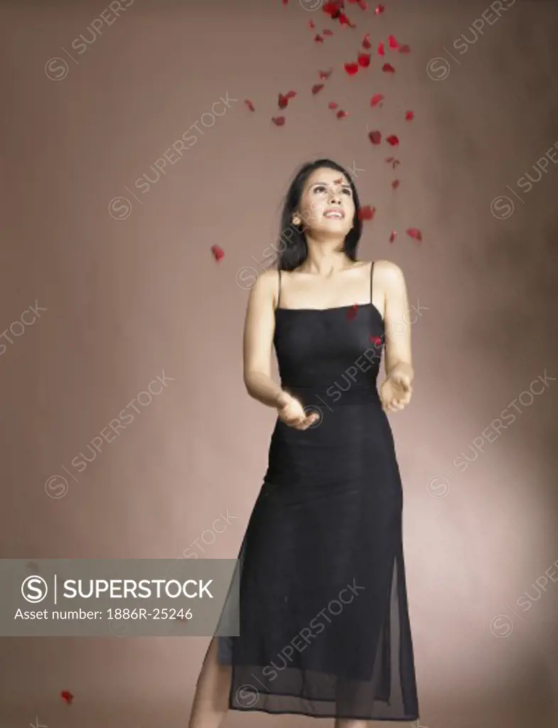 South Asian Indian woman throwing rose petals in air wearing black dress with brown background MR # 702