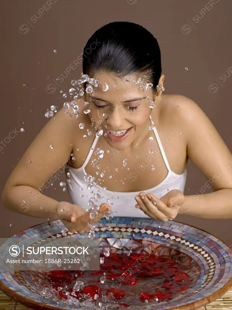 South Asian Indian woman splashing rose petals water on her face wearing white top MR # 702