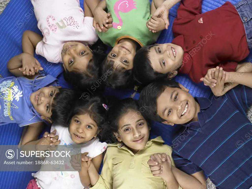 South Asian Indian boys and girls lay down on floor and holding hands in nursery school MR