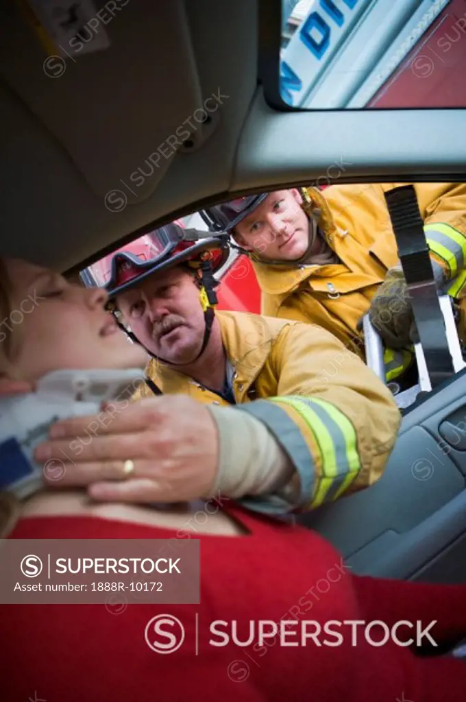 Fireman helping woman with neck brace while another fireman uses the jaws of life on a car door selective focus