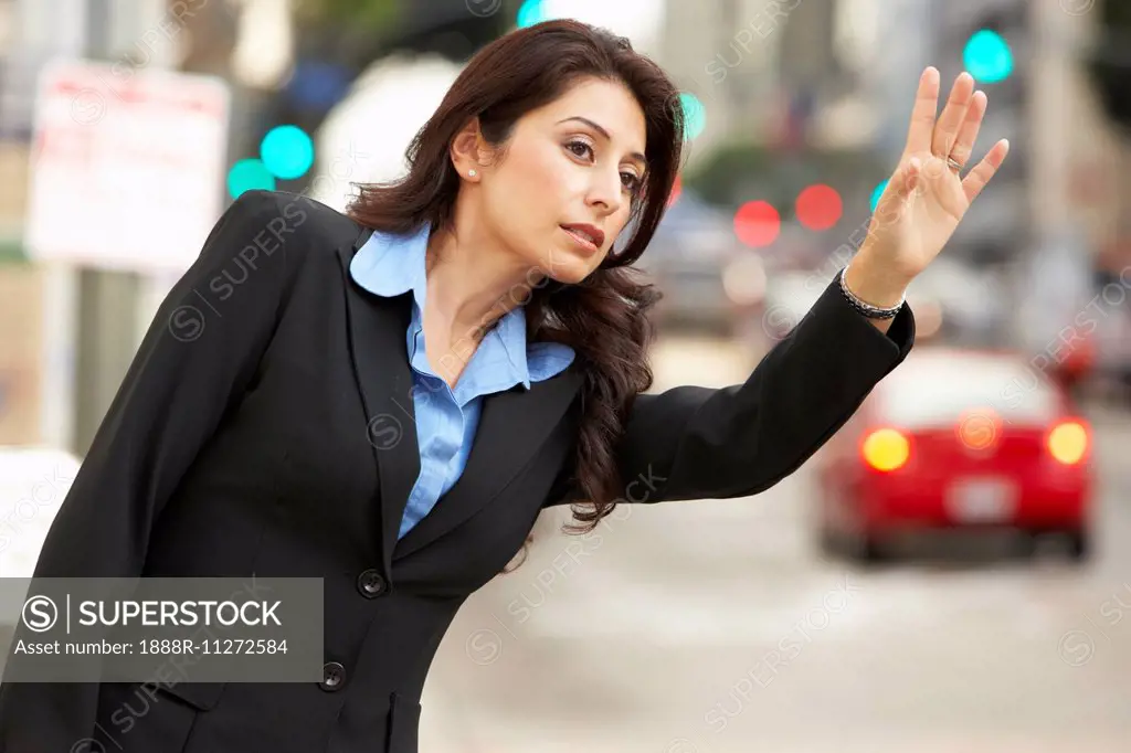 Businesswoman Hailing Taxi In Busy Street