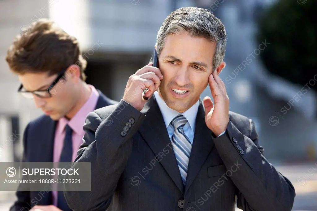 Businessman Speaking On Mobile Phone In Noisy Surroundings