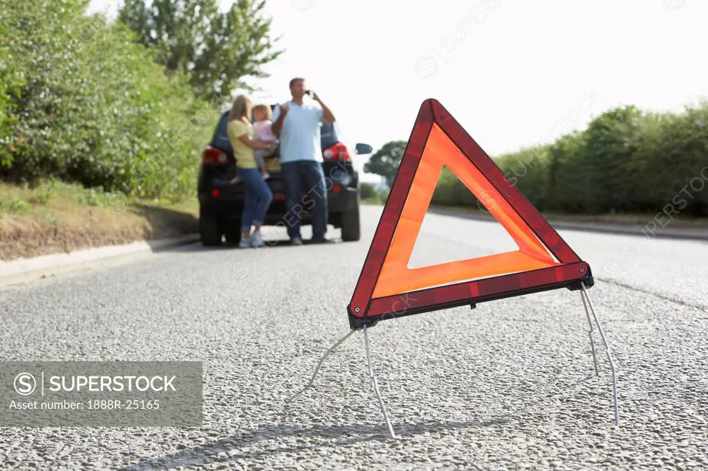 Family Broken Down On Country Road With Hazard Warning Sign In Foreground